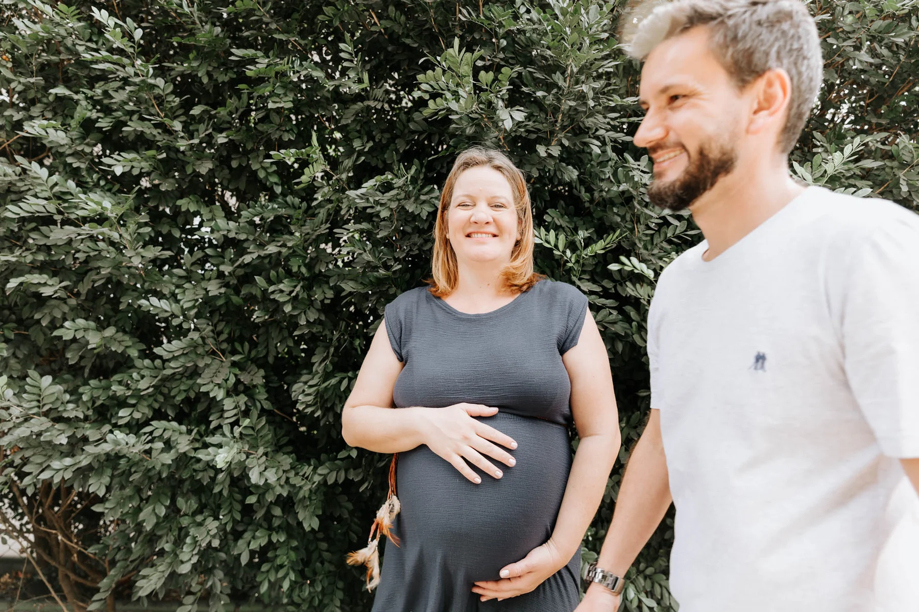 Expecting mother and partner smiling together outdoors, hand on the belly